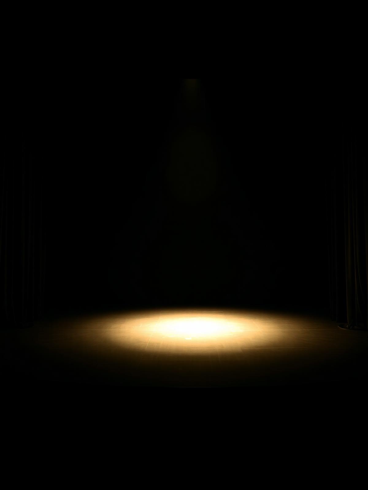 Minimalist empty theatre stage illuminated by a single gold spotlight